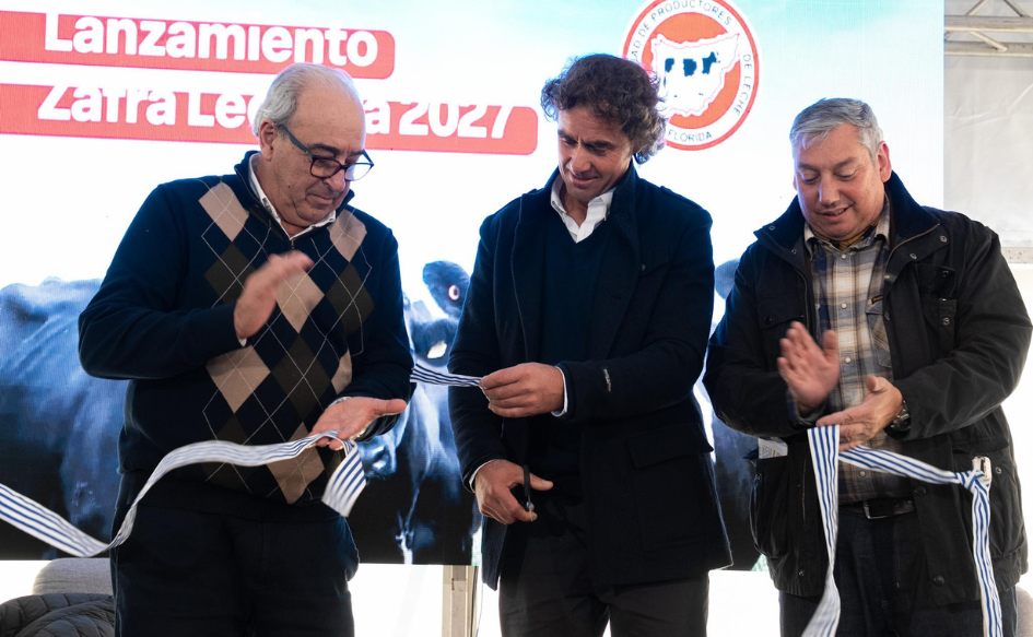 Presidente de la Sociedad de Productores de Leche de Florida, Fernando Lugea, le da un trozo de cinta de inauguración al ministro de Ganadería, Alfredo Fratti. A su lado, el intendente de Florida, Carlos Enciso, aplaude.