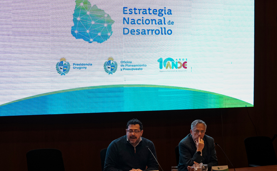 Secretario de Presidencia, Alejandro Sánchez, habla en un escenario. A su lado, el director de OPP, Rodrigo Arim, lo escucha con su mano apoyada en la boca. Atrás, un mapa de Uruguay con la leyenda "Estrategia Nacional de Desarrollo" y los logos de Presidencia, OPP y ANDE