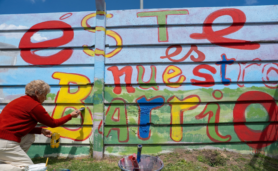 Vecina de Cerro Norte, de unos 60 años de edad, pinta el muro de la plaza de deportes n°10, en el que se lee "Este es nuestro barrio"