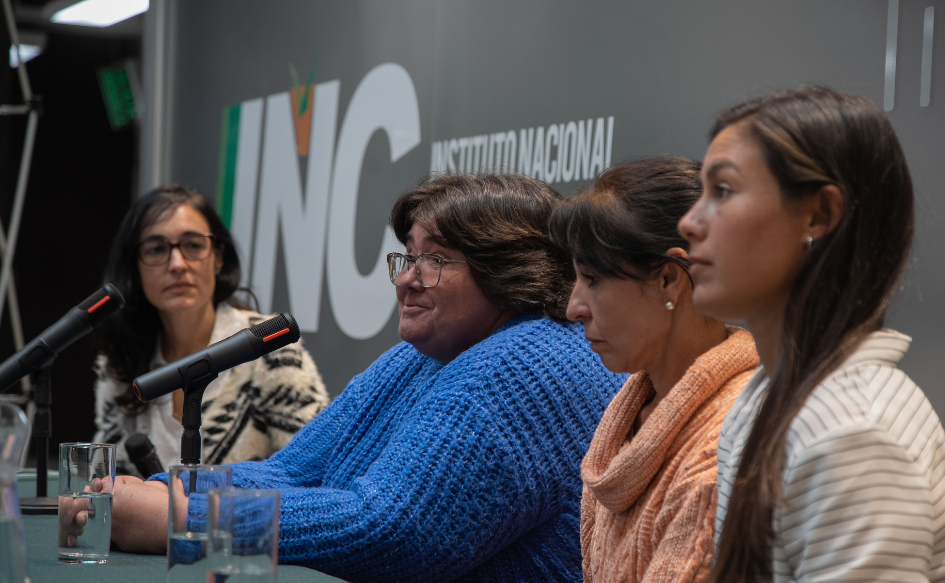 Cuatro mujeres hablan en conferencia. Detrás, un banner con el logo del Instituto Nacional de Colonización