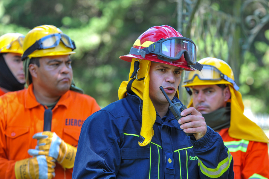 Bombero habla por un transmisor portátil, mientras dos bomberos lo observan atentamente