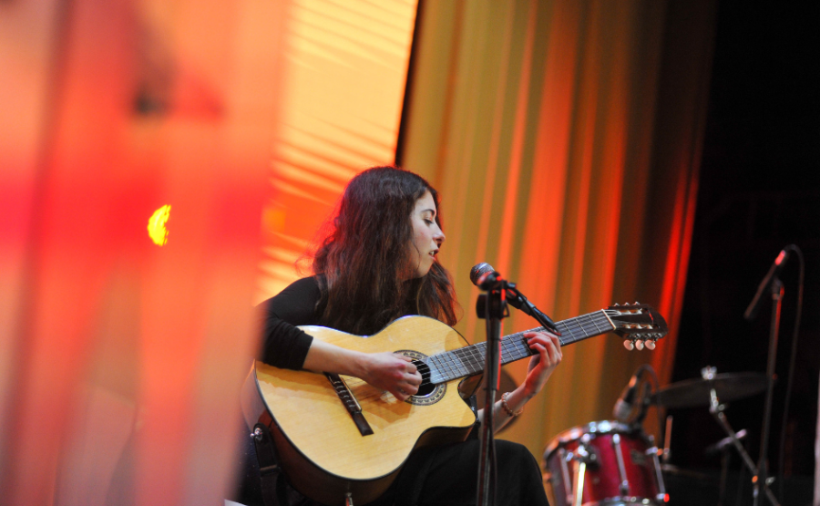 Mujer de unos 20 años toca la guitarra en el escenario de un teatro