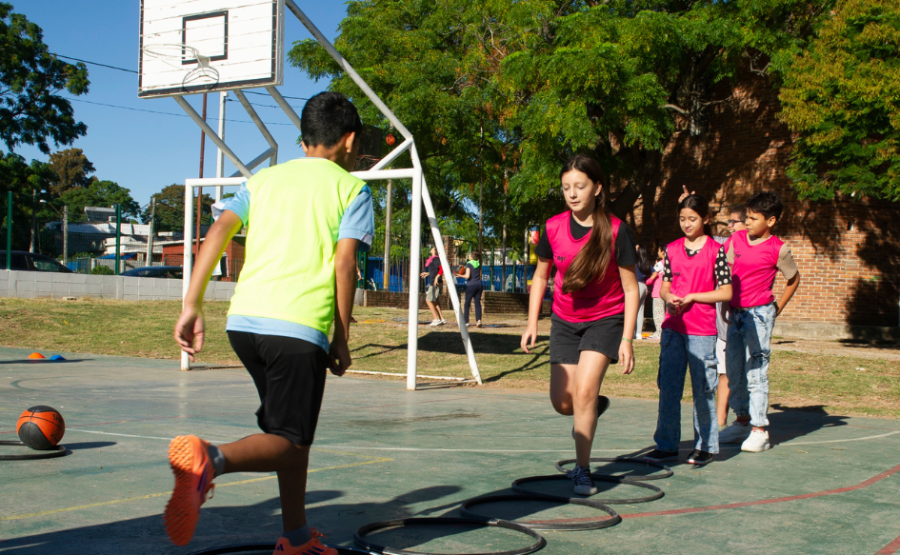 Un niño y una niña de unos 10 años saltan en un pie sobre unos aros colocados en el piso de una cancha de básquetbol