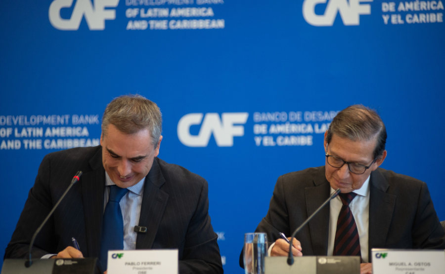 Presidente de OSE, Pablo Ferreri, sonriente, firma el contrato de financiamiento. A su lado, el representante de CAF en