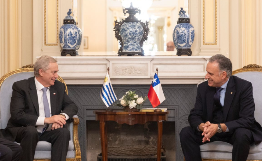 Presidentes de Uruguay, Yamandú Orsi, y Chila, José Kast, sentados, conversan sonrientes. En medio de ellos, el pabellón
