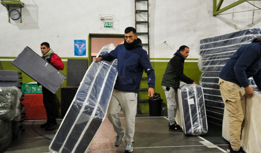 Personas cargando colchones en centro de evacuación 