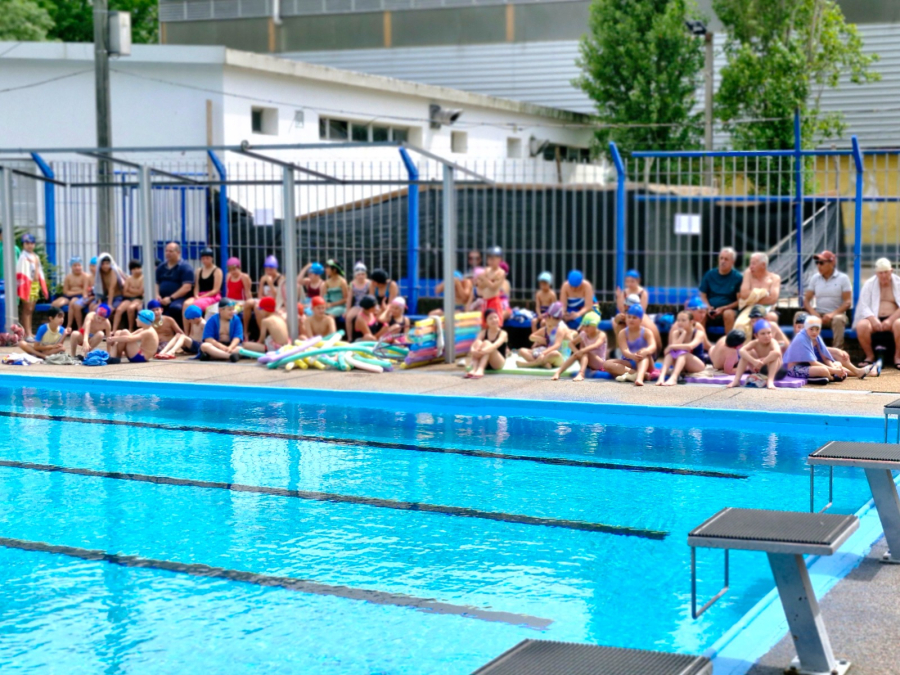 Piscina en plaza de deportes. En el borde, muchos niños sentados.