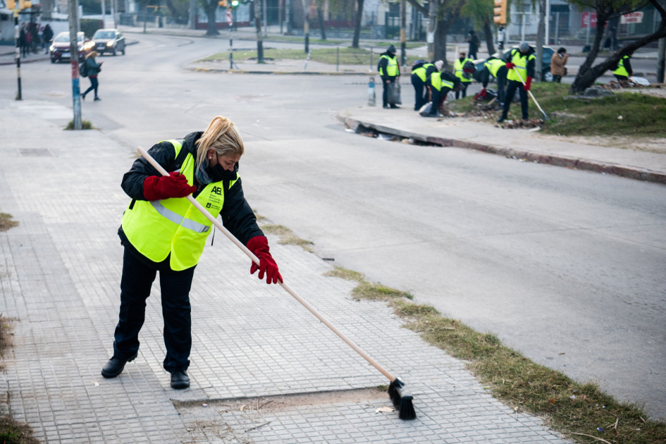 Personas con chalecos refractarios barriendo veredas y cordones