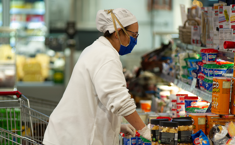 Trabajadora, con una cofia y tapabocas, ordena productos en la góndola de un comercio