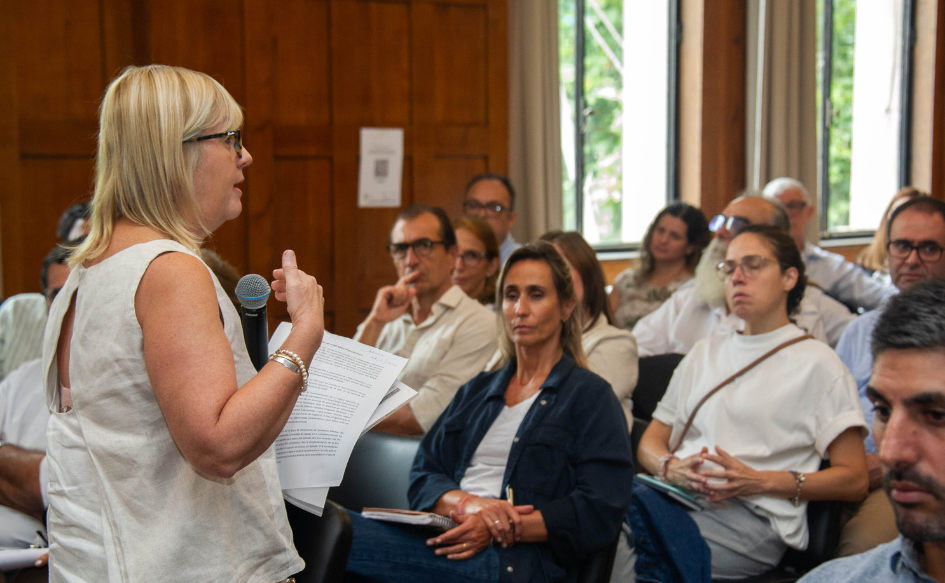Ministra de Saluda Pública, Cristina Lustemberg, habla a personas que están sentadas, con un micrófono en la mano