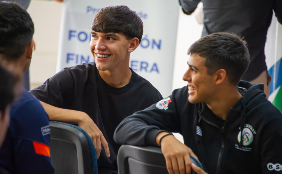 Dos jóvenes del programa Pelota al Medio a la Esperanza, sentados en una silla, miran hacia atrás y sonríen