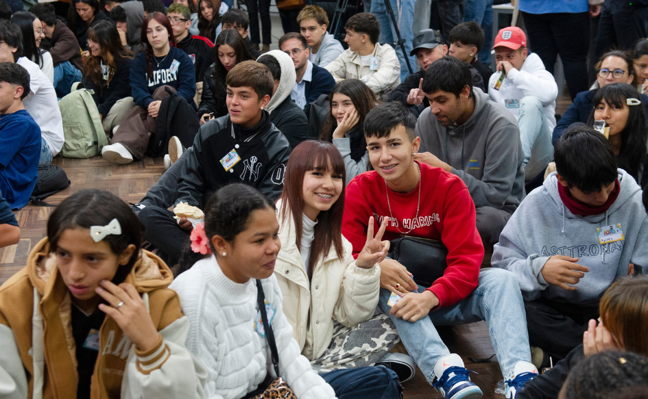 Decenas de adolescentes están sentados en el piso, en la sede del INJU. Dos de ellos, observan a la cámara sonrientes y con los dedos índice y mayor levantados, formando una "v"
