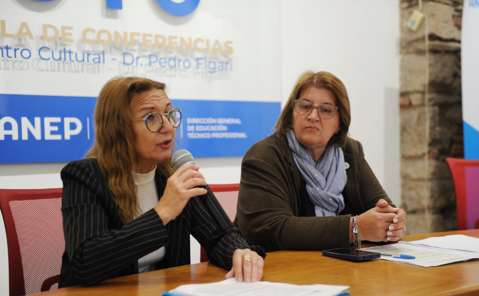 Directora del INR, Ana Juanche, habla con un micrófono en la mano. A su lado, la observa la directora de UTU, Virginia Verderese