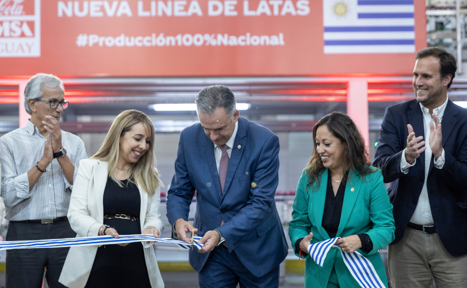 Presidente Orsi corta cinta de inauguración en la línea de producción de latas de Coca Cola Femsa. A su lado, los ministros de Industria y Trabajo, y representantes de la empresa. De fondo, un cartel con la leyenda: "Nueva línea de latas #Producción100%Nacional", al lado de una bandera de Uruguay