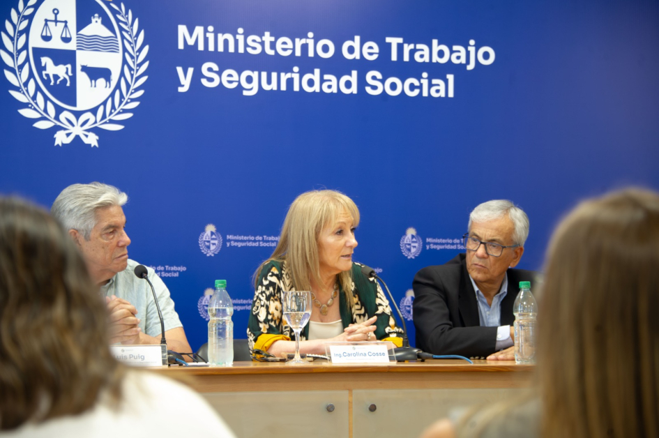 Presidenta en ejercicio, Carolina Cosse, habla en una mesa integrada por el ministro de Trabajo y Seguridad Social, Juan Castillo, y el inspector Luis Puig. Detrás, un back con el logo del Ministerio de Trabajo