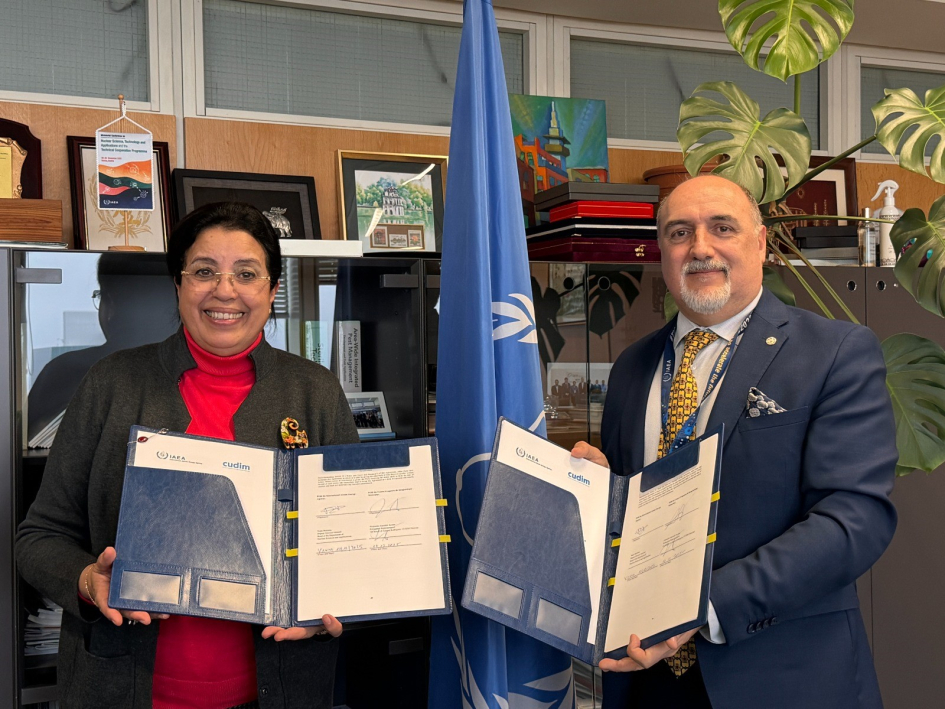 El embajador de Uruguay en Austria, Alejandro Garofali, y la directora general adjunta y jefa del Departamento de Ciencias y Aplicaciones Nucleares de OIEA, Najat Mokhtar, sostienen una carpeta con un documento firmado.