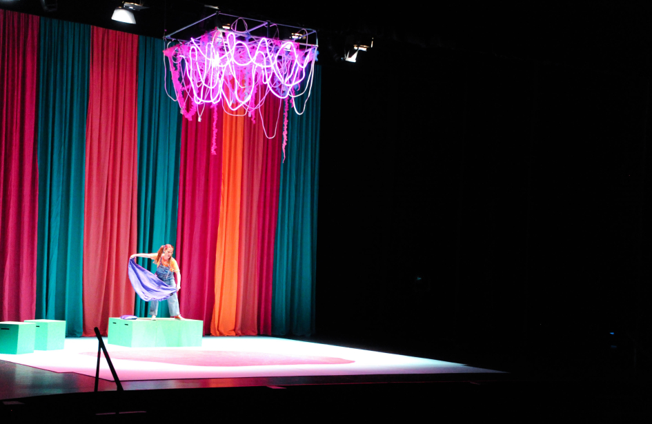 Mujer actúa en el escenario de un teatro. Detrás, un telón de colores