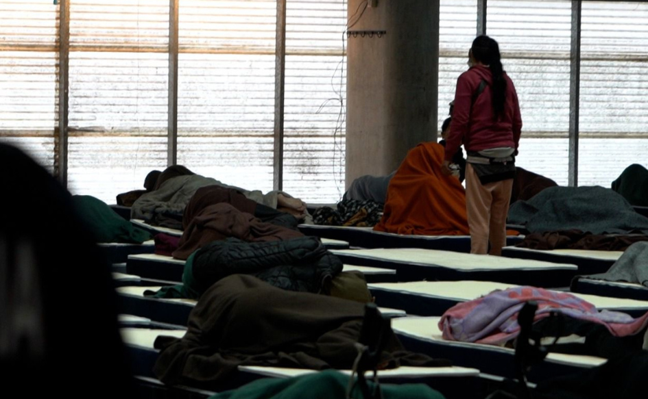 Alerta por frío extremo: 3.707 personas en situación de calle fueron asistidas el sábado 4 de julio Una persona de pie entre varias camas dispuestas en fila en el polideportivo de la Escuela Nacional de Policía