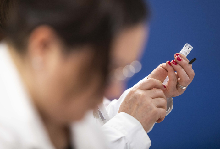 Primer plano de las manos de una mujer con túnica blanca preparando una inyección con jeringa y vial