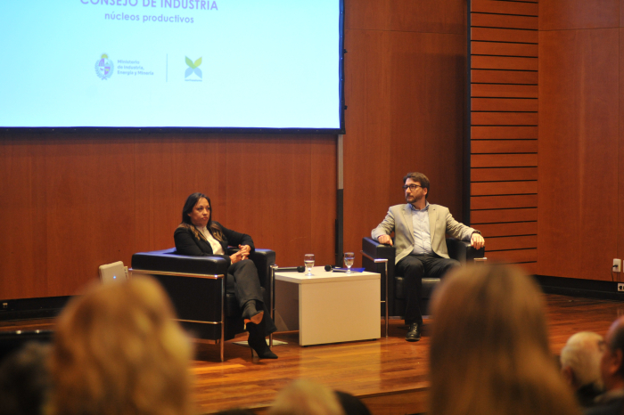 Ministra de Industria junto al director nacional de Industrias sentados en sillones en escenario.
