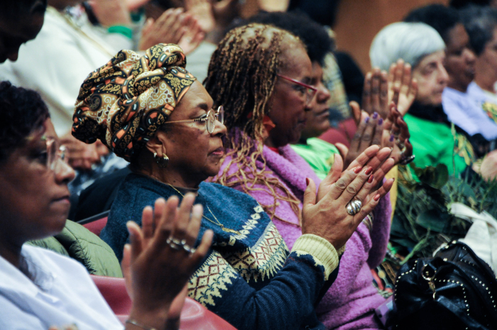 Mujeres afrodescendientes aplauden sentadas en primera fila de la platea del auditorio.