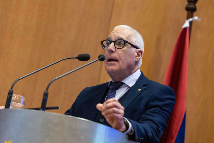 Ministro del Interior diserta parado en atril con micrófono en el escenario del auditorio.