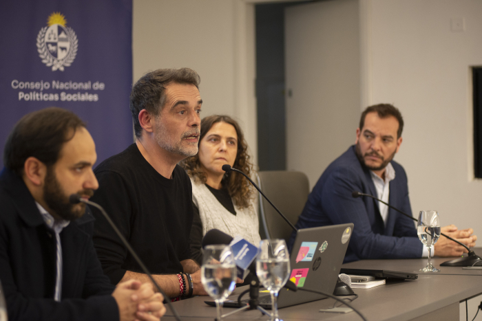 Ministro de Desarrollo Social diserta frente a un micrófono, en una mesa, junto a otras autoridades.