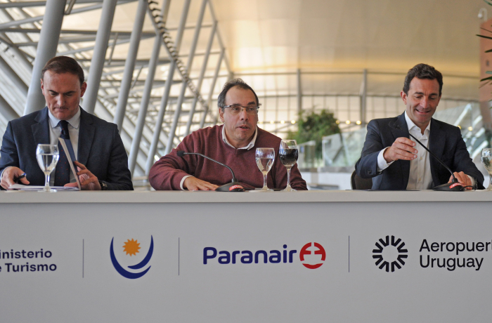 Ministro de Turismo y representantes de la aerolínea Paranair sentados en mesa con micrófonos.