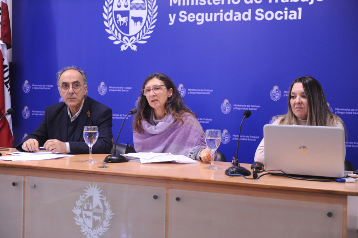 Funcionaria del ministerio diserta en mesa con micrófono junto Barreto y otra funcionaria. 
