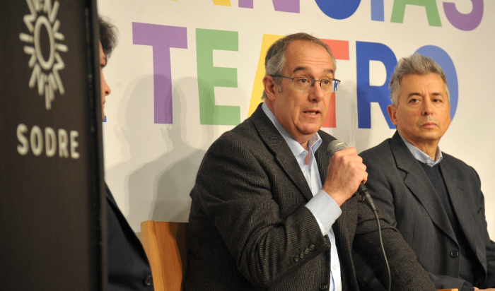 Ministro de Educación y Cultura diserta sentado con micrófono en mano.