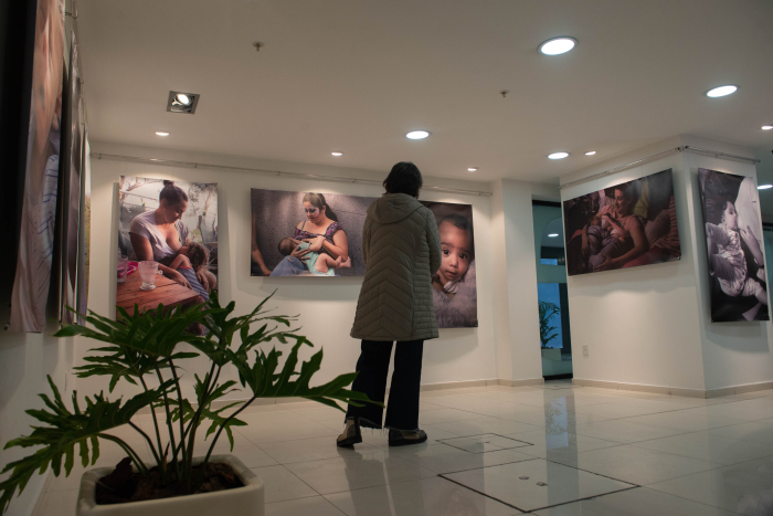 Una mujer de espaldas observa una exposición de fotos en el hall de la sede de ASSE.