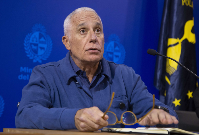 Ministro del interior diserta sentado en una mesa con micrófono en sala de conferencias 