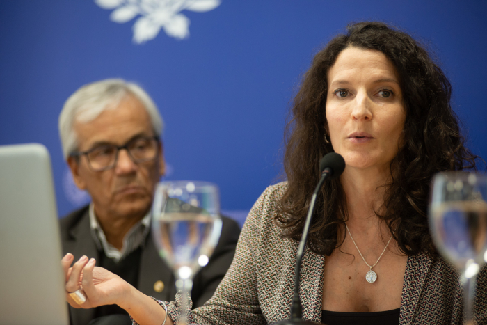 Mujer diserta sentada en mesa con micrófono junto al ministro de Trabajo. 