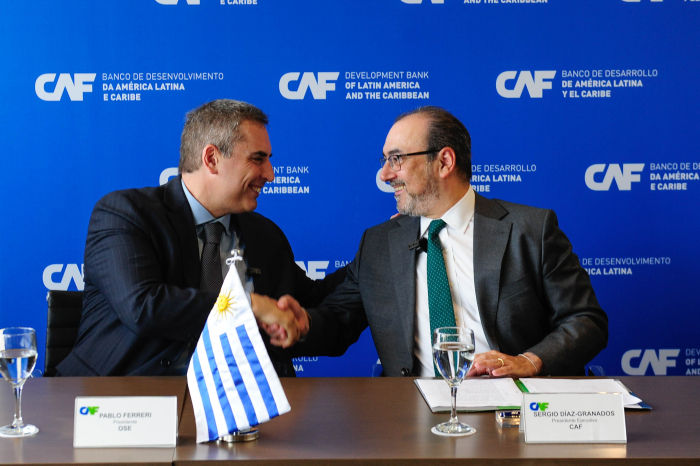 Los presidentes de OSE y de CAF se estrechan la mano sentados en mesa.