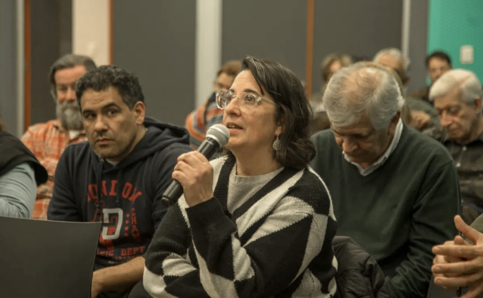 Una mujer, sentada entre el público, diserta con micrófono en mano.