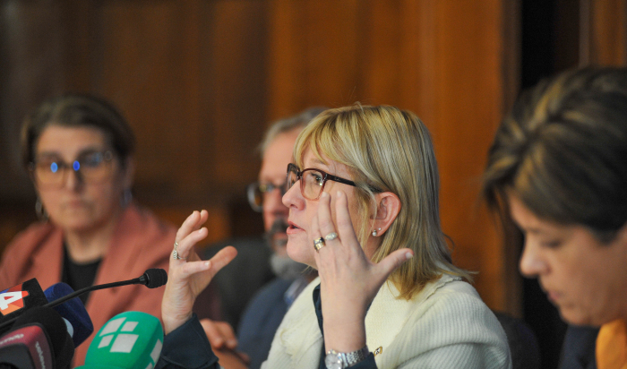 Ministra de Salud Pública, de perfil, diserta sentada en mesa con micrófono