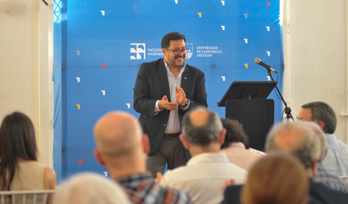 Secretario de Presidencia, de pie en un estrado, sonríe y aplaude frente al público. 