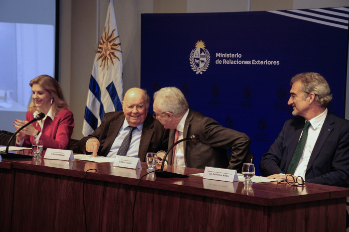 El canciller dialoga con el presidente de la Fundación Astur sentados en mesa con micrófonos. 