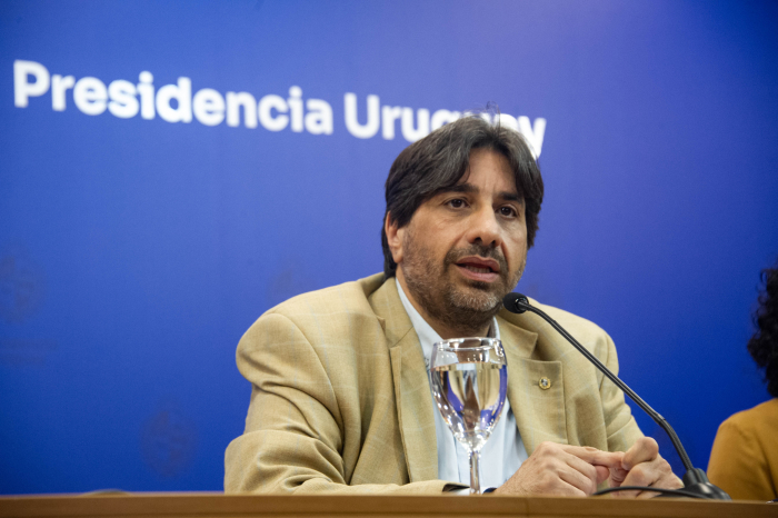 Presidente de la Unasev diserta sentado en mesa con micrófono, en sala de conferencia.
