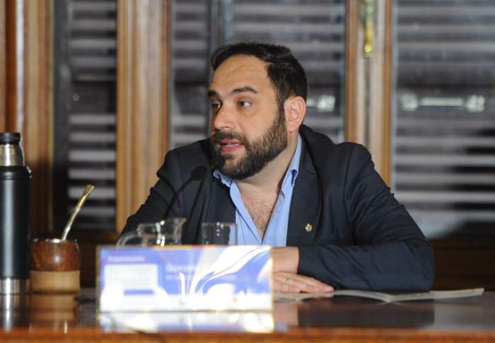 Titular del Ministerio de Desarrollo Social diserta, sentado en mesa de madera