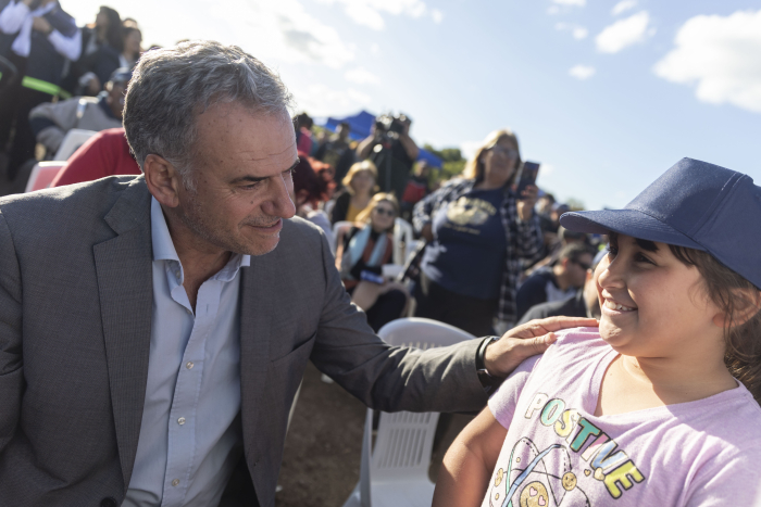 Orsi y una niña con gorra azul sonríen mientras conversan al aire libre