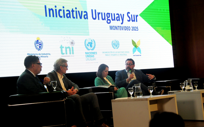 Secretario de Presidencia diserta sentado con micrófono en mano en el escenario del auditorio.