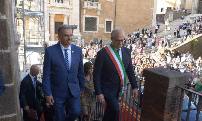 Orsi y el alcalde de Roma, con una banda tricolor sobre su traje, conversan sentados en una oficina.
