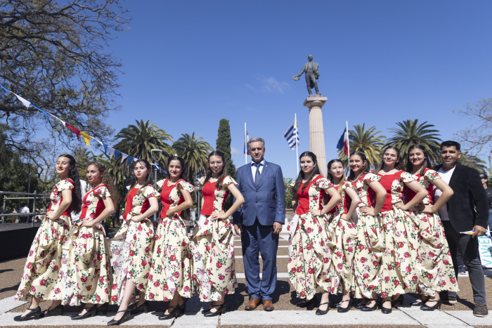 Presidente Orsi posa junto a un grupo de danza folclórica con vestimenta tradicional en la plaza.