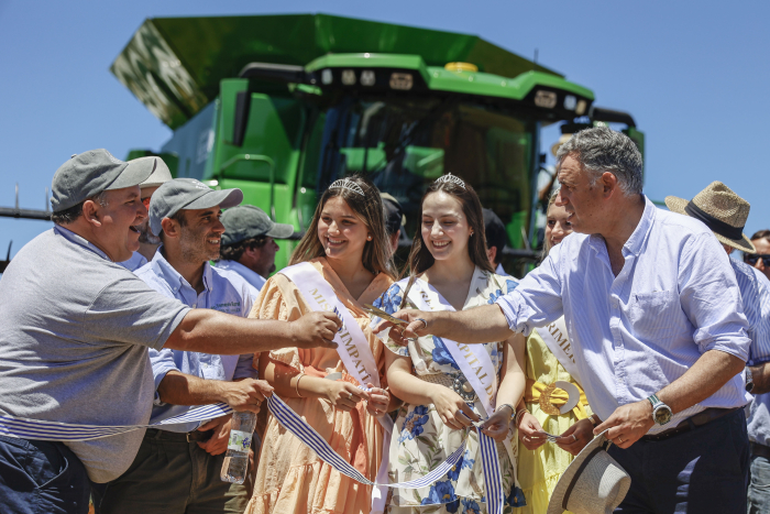Orsi y otro hombre cortan una cinta de inauguración. En el medio están las “reinas de la cosecha”. 