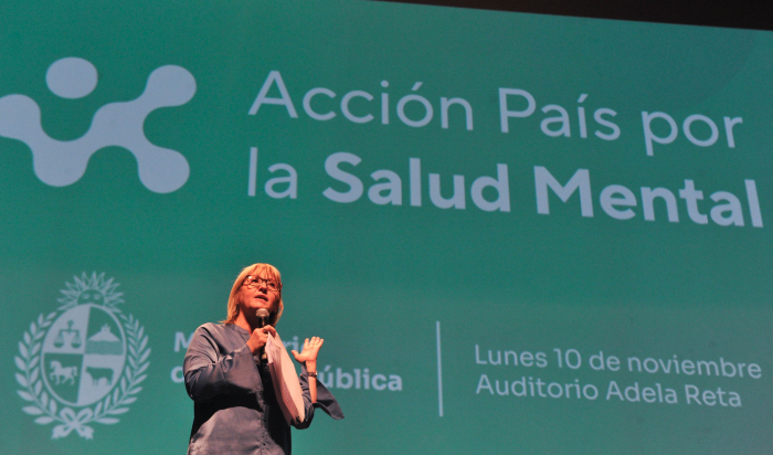 Ministra de Salud Pública de pie en un escenario diserta con micrófono en mano.