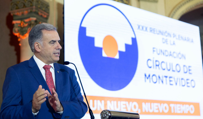 Orsi diserte, de pie, en atril con micrófono.