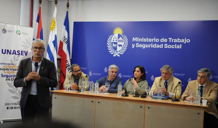 Ministro de Trabajo diserta de pie con micrófono en mano. Atrás las autoridades sentadas.