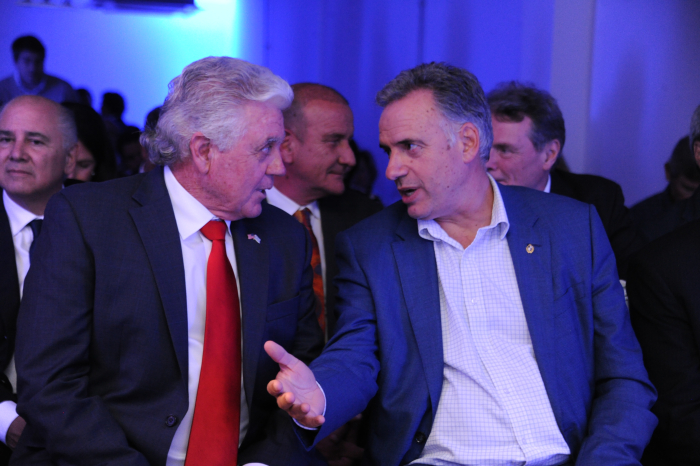 Primer plano de Orsi, sentado en la platea, dialogando con el embajador de Estados Unidos. 