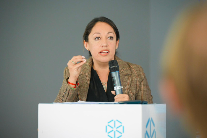 Ministra de Industria diserta con micrófono en mano en un atril blanco.